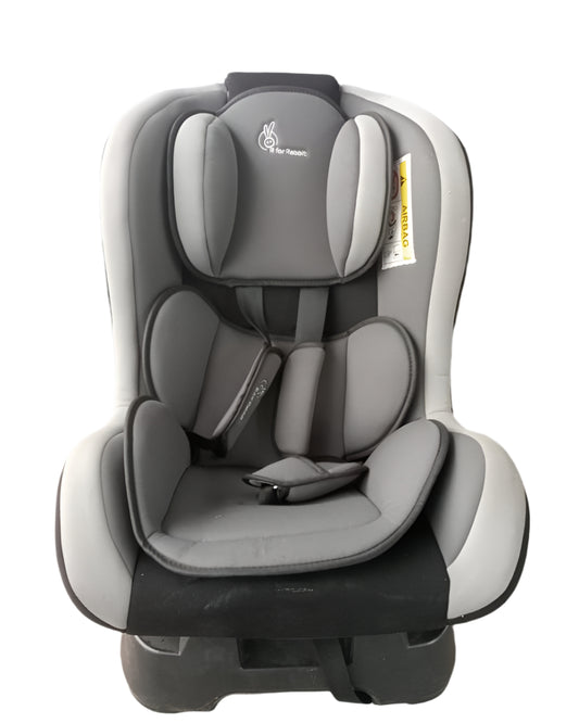 Gray and black car seat in front of a gray vehicle on a concrete surface