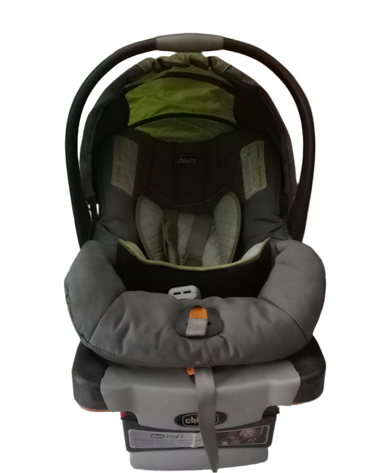 Gray and green car seat on a white floor with a wooden door in the background