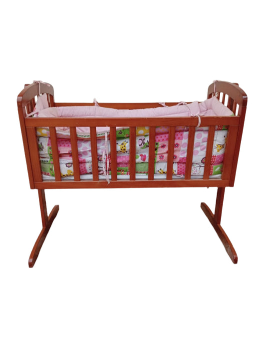 Wooden baby crib with pink bedding on a stone floor