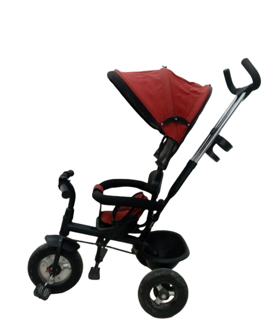 Red and black baby tricycle against a neutral curtain background